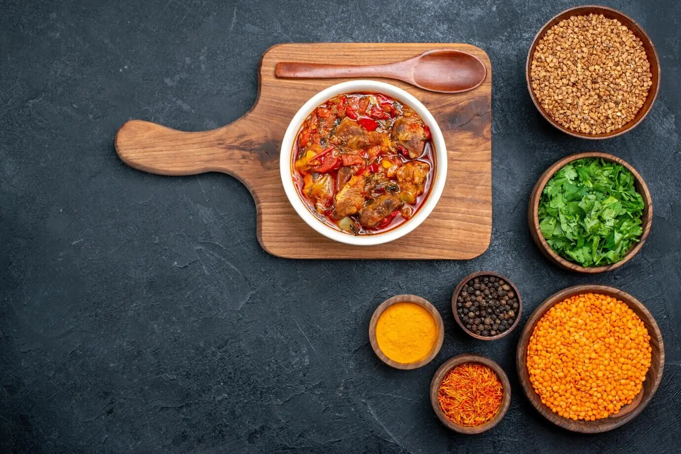 Draufsicht auf eine köstliche Gemüsesuppe mit Gewürzen und Kräutern auf dunklem Untergrund.